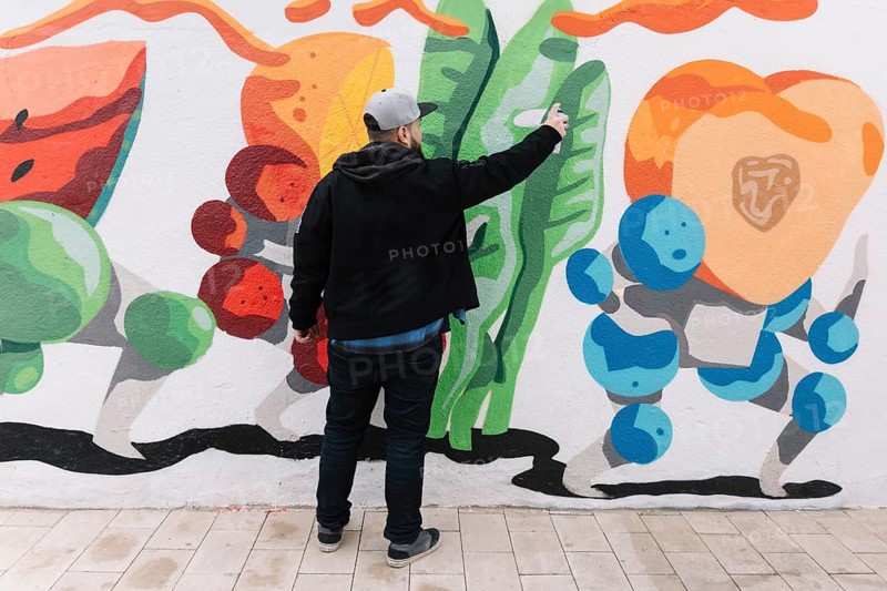 Rear view man making graffiti with spray can wall