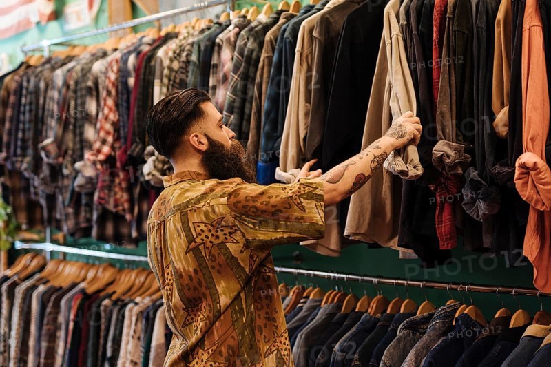 Young man looking shirt hanging rail inside clothing shop