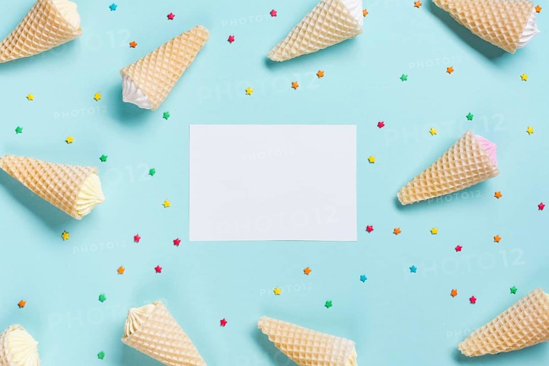 Overhead view waffle cones sprinkles surrounded near white blank paper blue backdrop