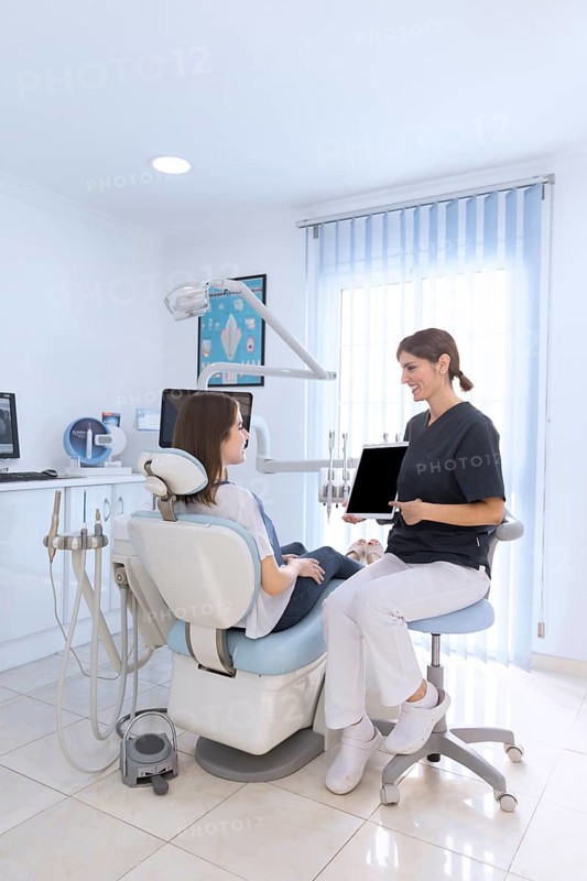 Female dentist pointing digital tablet screen patient sitting chair clinic