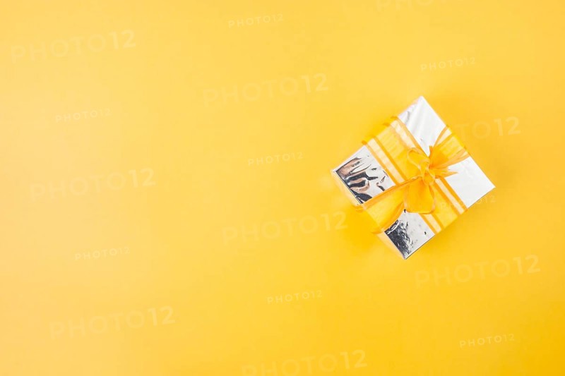 Silver gift box decorated with yellow ribbon yellow background