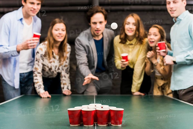 Friends looking ball while man playing beer pong bar