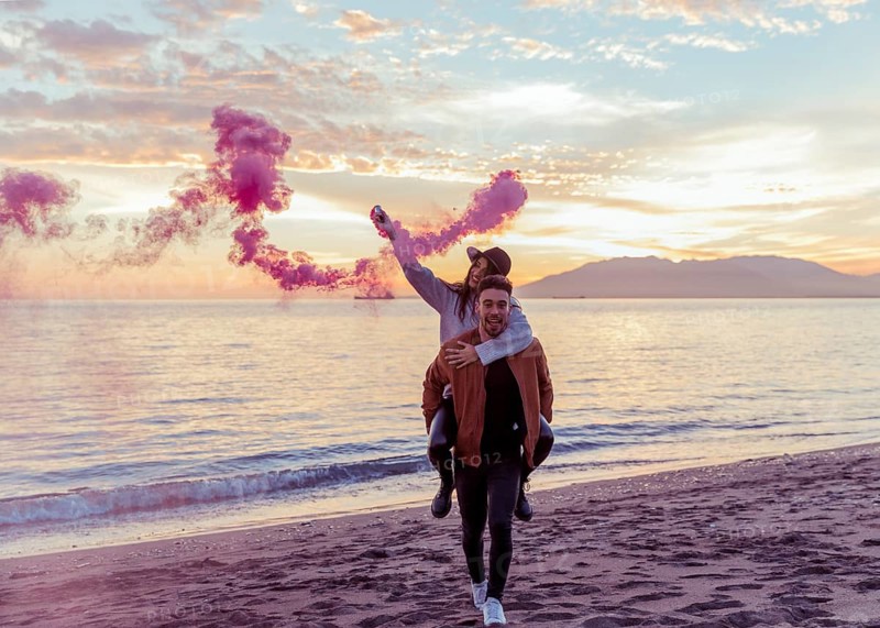 Man holding woman with pink smoke bomb back sea shore