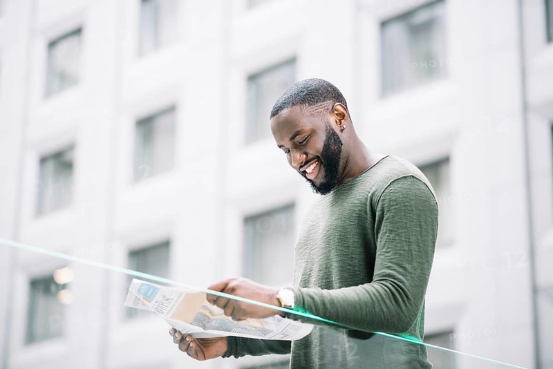 Smiling man reading newspaper near glass fence
