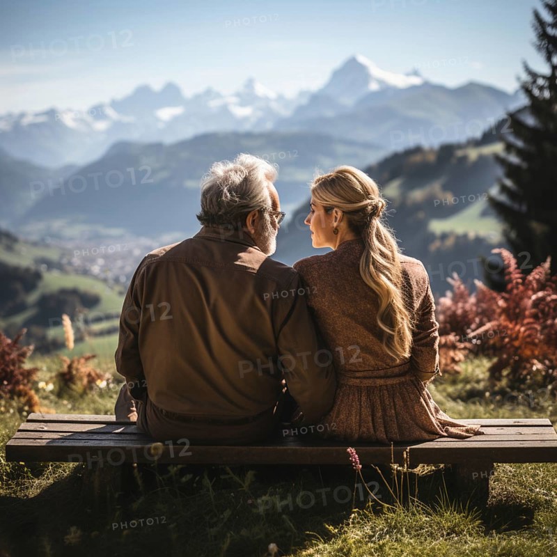 Retired couple sitting on a bench in the mountains and looking at the mountain panorama
