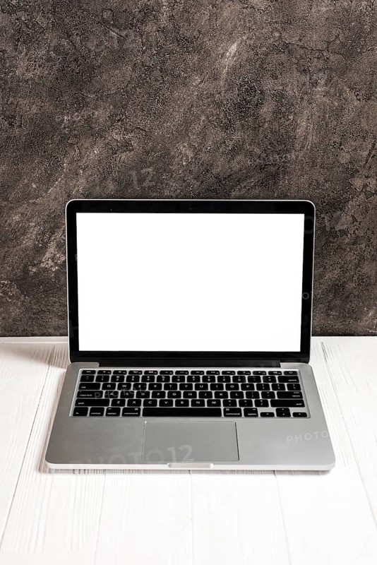 Laptop with blank white screen white wooden table against concrete