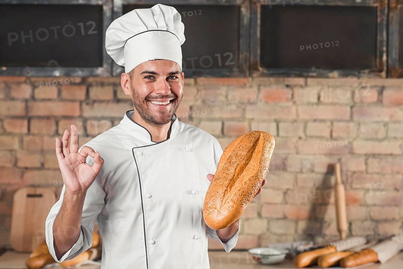 Smiling male baker holding loaf showing ok hand sign gesture