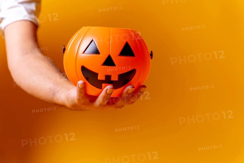 Hand holding an orange Halloween pumpkin on a background of yellow