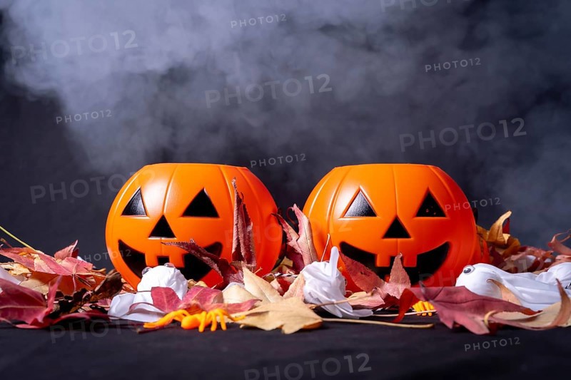 Detail of Halloween pumpkins over red autumn leaves and ghosts with smoke on a black background