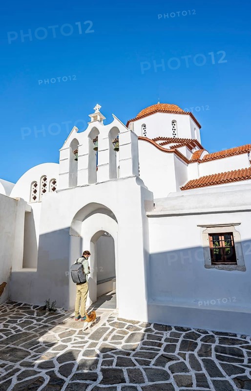 Young man with cat in front of archway with bells of Agios Antonios chapel and Greek Orthodox church Metamorfosi Sotiros