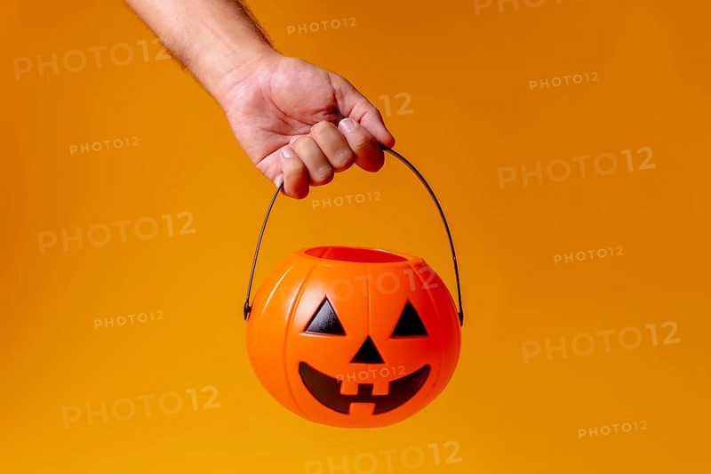 Hand holding an orange Halloween pumpkin on a background of yellow
