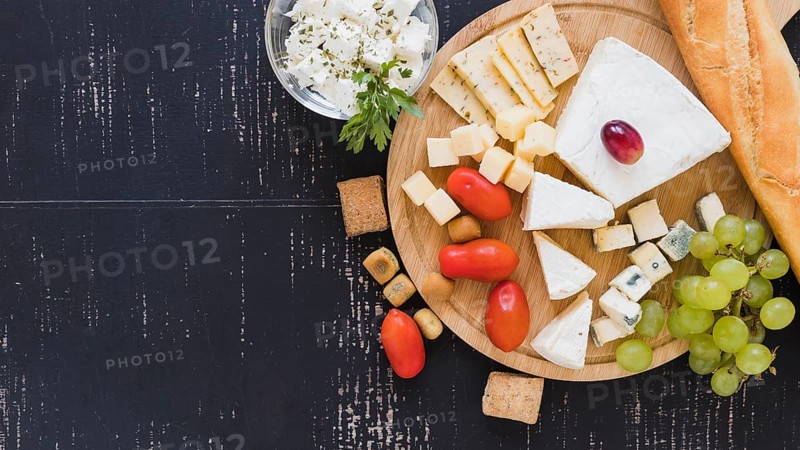 Cherry tomatoes grapes cheese blocks baguette round chopping board textured backdrop
