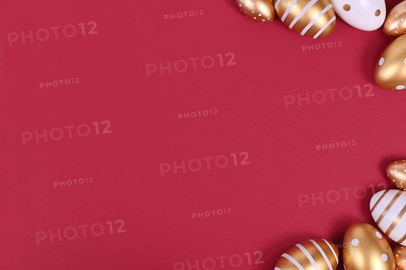 Flat lay with golden and white easter eggs painted with stripes and dots in corners of dark red background with blank copy space