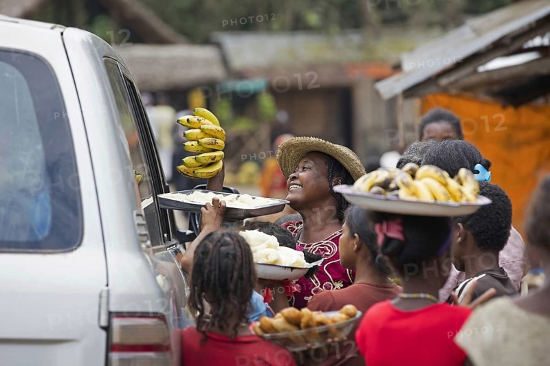 Local Malagasy women selling bananas and food to passers-by traveling in vehicle in rural village in Madagascar