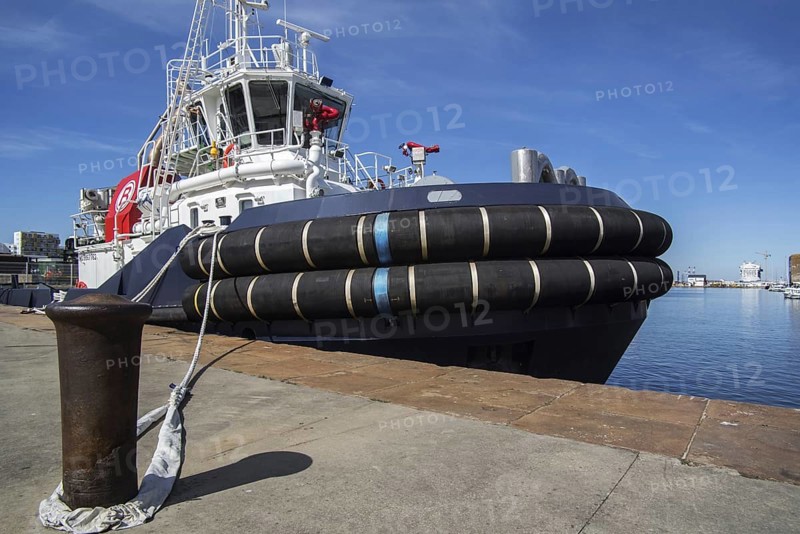 Mooring bollard and the French tug boat VB Mirage showing huge tugboat fenders docked in the seaport of Saint-Nazaire
