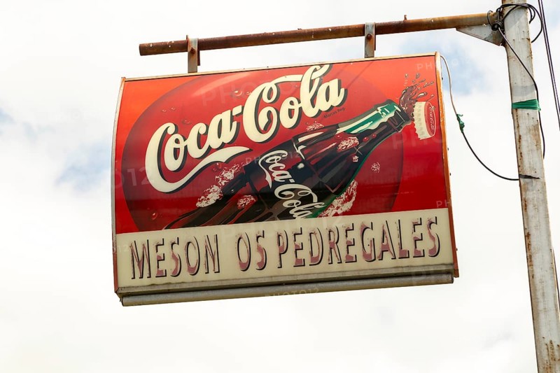 Cafe Coca-Cola drink sign from below against white cloudy sky