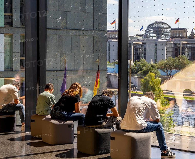 Museum visitors sitting at the window of the Futurium using their smartphones