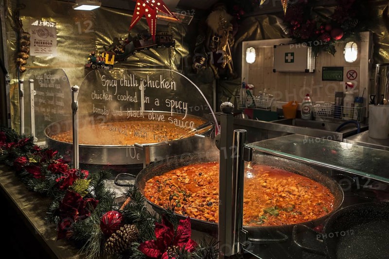 Large pans with simmering spicy chilli chicken for sale in stall during evening Christmas market in winter