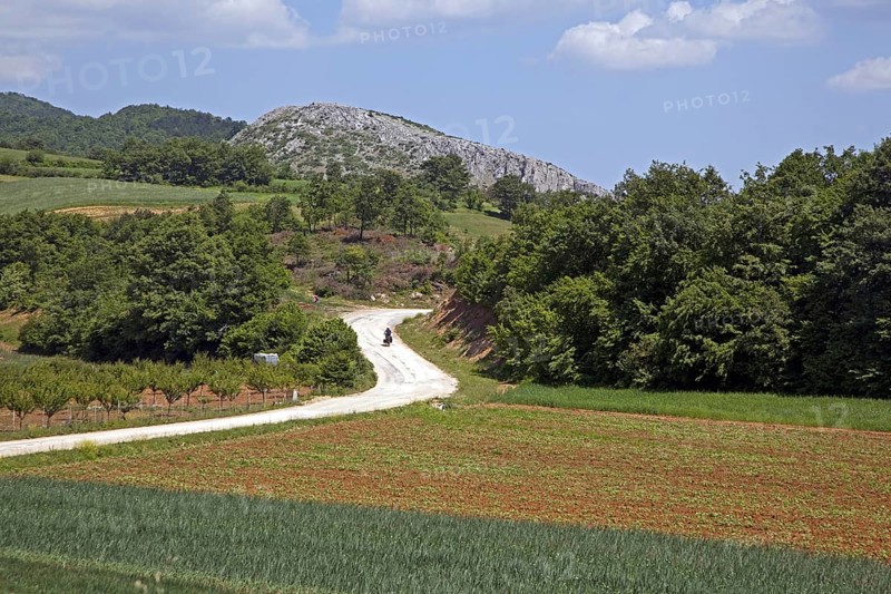 Touring cyclist cycling on winding dirt road along fields in rural Western Turkey