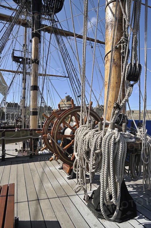 Steering wheel and ropes coiled around belaying pins aboard the Grand Turk