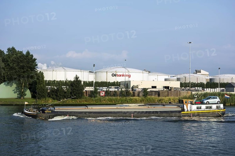 Inland vessel sailing past storage tanks of Oiltanking Ghent
