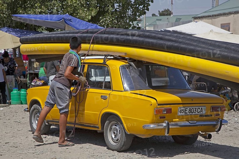 Uzbek boy fixing large pipes on top of old Trabant in Uzbekistan