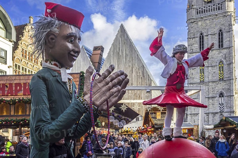 Puppeteer and street performer performing balancing act on giant ball during Christmas market in winter in Ghent