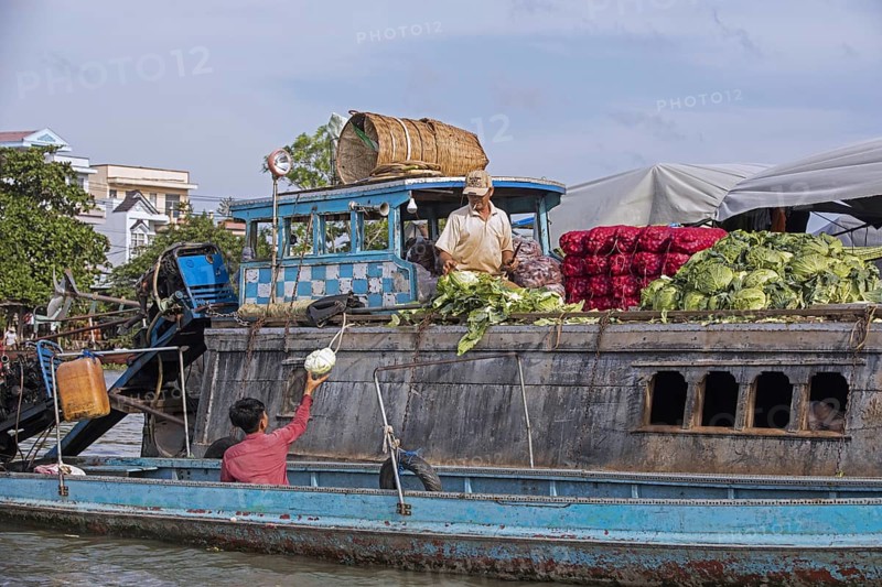 Vietnamese farmer selling vegetables from traditional wooden boat at the floating market of the city Can Tho in the Mekong Delta