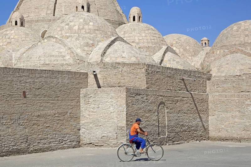 Uzbek man cycling in front of mosque in the ancient historic city of Bukhara