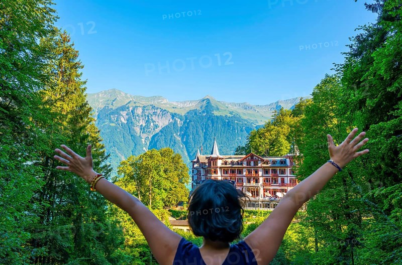Woman with Arms Outstretched in Front of The Historical Grandhotel Giessbach on the Mountain Side in Brienz