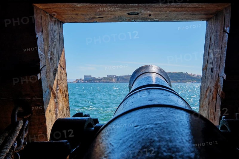 Sea view out of a gunport in hull of the ship over the gun cannon muzzle in on the gun deck of a sailing ship of Age of Sail