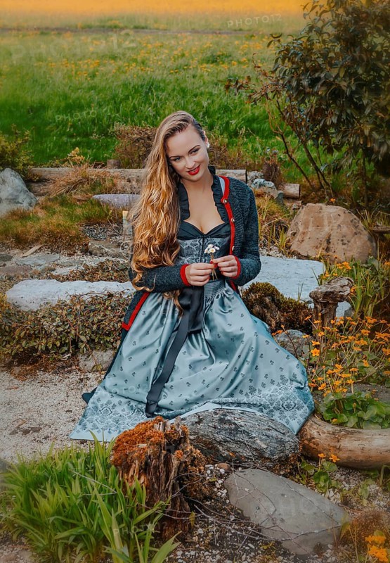 Woman in festive dirndl and flowers in hand