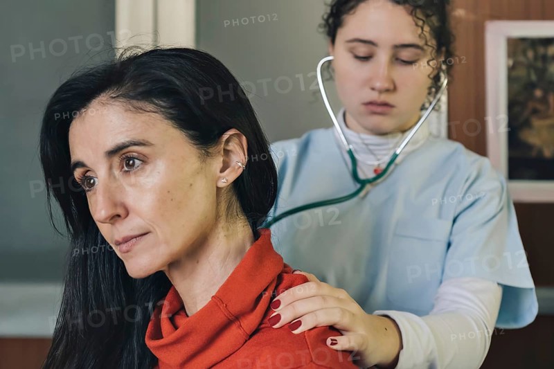 Young female physician performs a medical examination on a middle-aged patient. Lung auscultation for respiratory evaluation