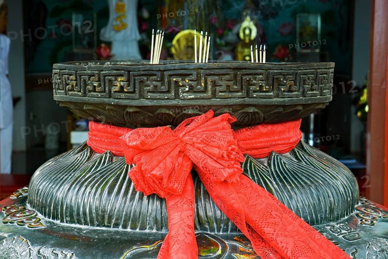 Red ribbon on a bowl for incense sticks in front of a pagoda