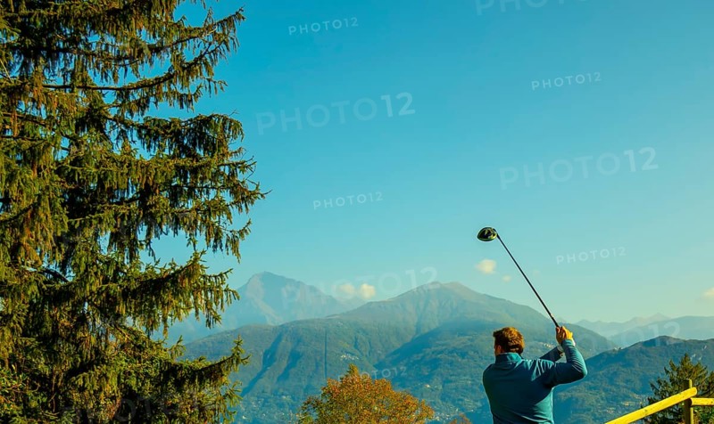 Golfer Teeing Off with His Driver with Mountain View in Autumn in Lombardy