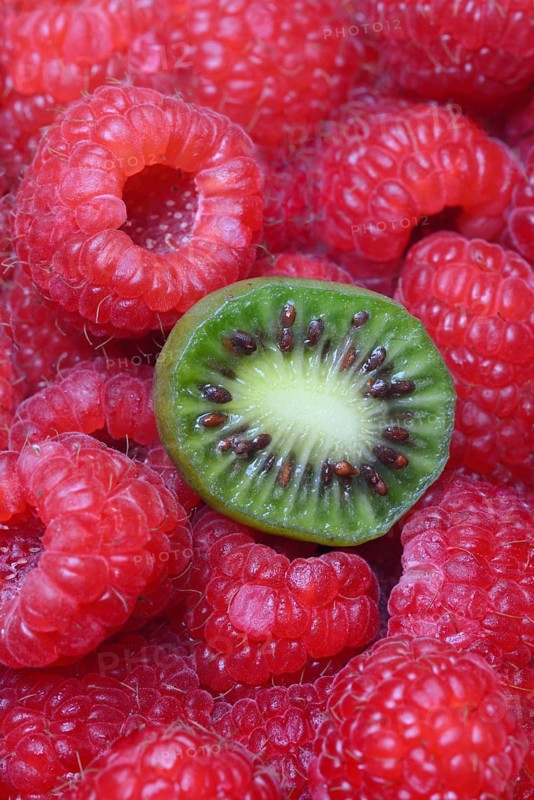 Halved mini kiwi on raspberries