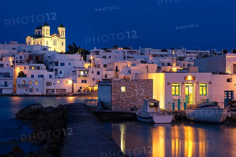 Traditional Greek whitewashed houses and church of Dormition of Mother of God on hilltop by seafront after sunset