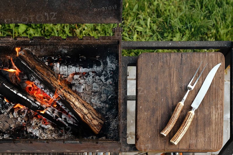 Top view of metal grill with burning log and fork and knife for steak