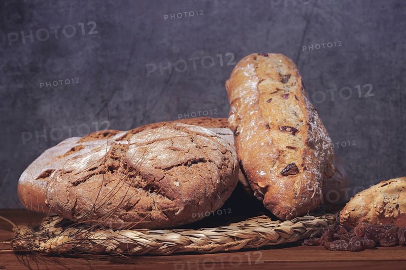 Loaf and loaves of rustic bread with ears of wheat on wooden table