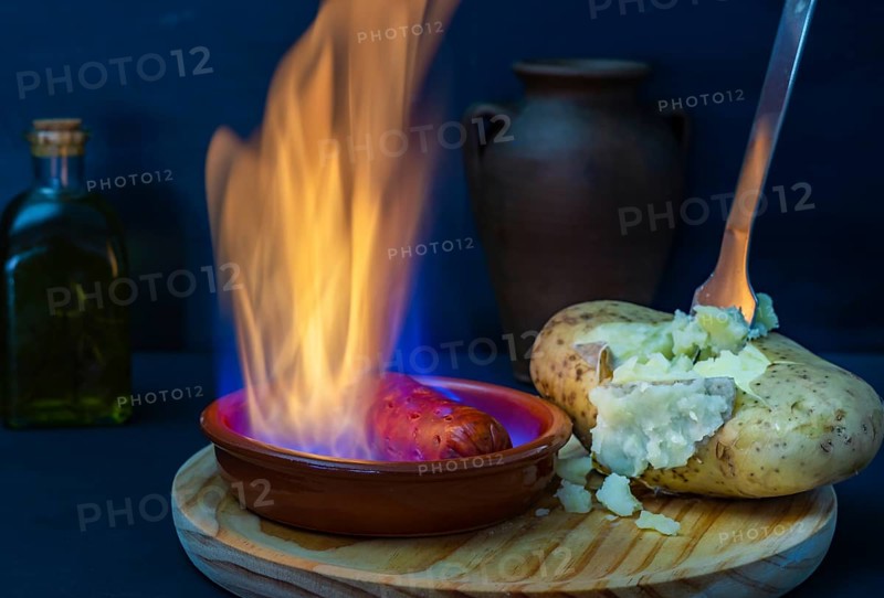 Boiled potato opened with a fork and chorizo in flames