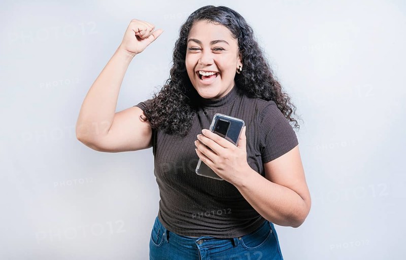 Winning happy young woman holding cell phone. Happy latin girl celebrating with phone isolated. Happy people holding smartphone and celebrating