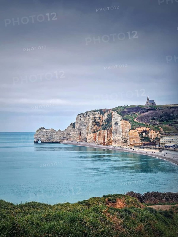Idyllic view to Etretat coastline with the famous Notre-Dame de la Garde chapel on the Amont cliff. Shore washed by Atlantic ocean waters