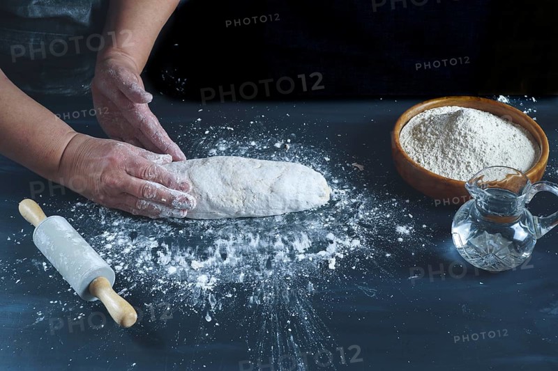 Woman kneading with her hands a flour dough to make homemade bread on a black wooden table with flour