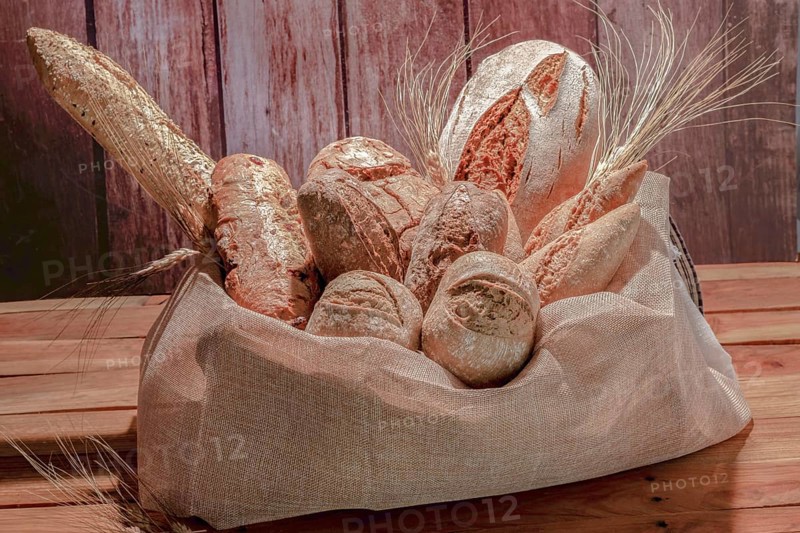 Different types of seed bread in a raffia sack on a wooden table with ears of wheat