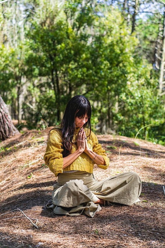 Woman with hands clasped meditating on the woods. Vertical Shot