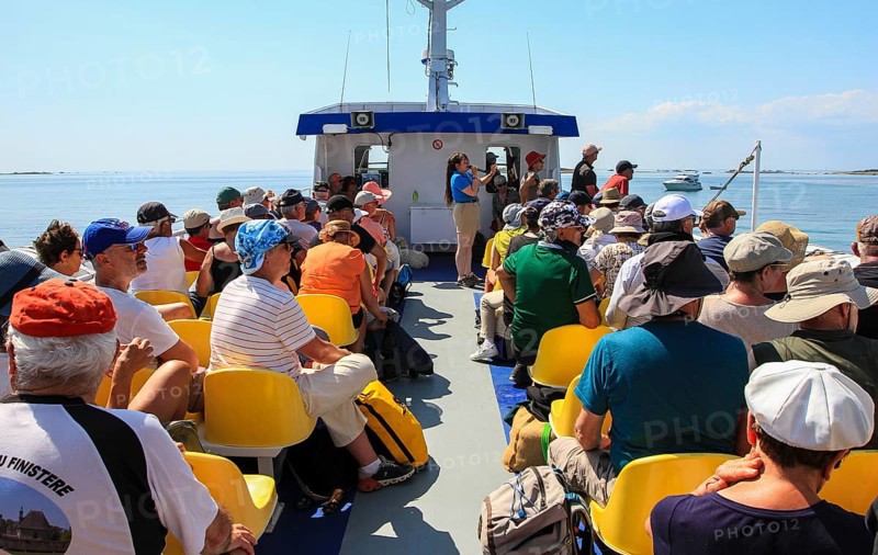 Sun deck of a tourist ship with tourists and crew member giving explanations via microphone