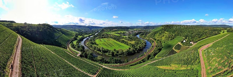 Wiltinger Saarbogen. The river winds through the valley and is surrounded by vineyards and green forests. Kanzem