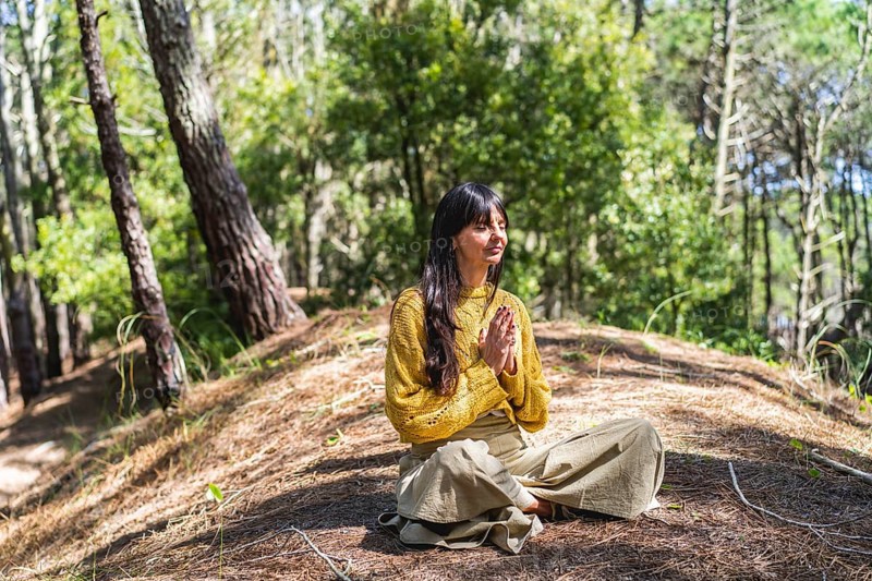 Woman with hands clasped meditating on the woods