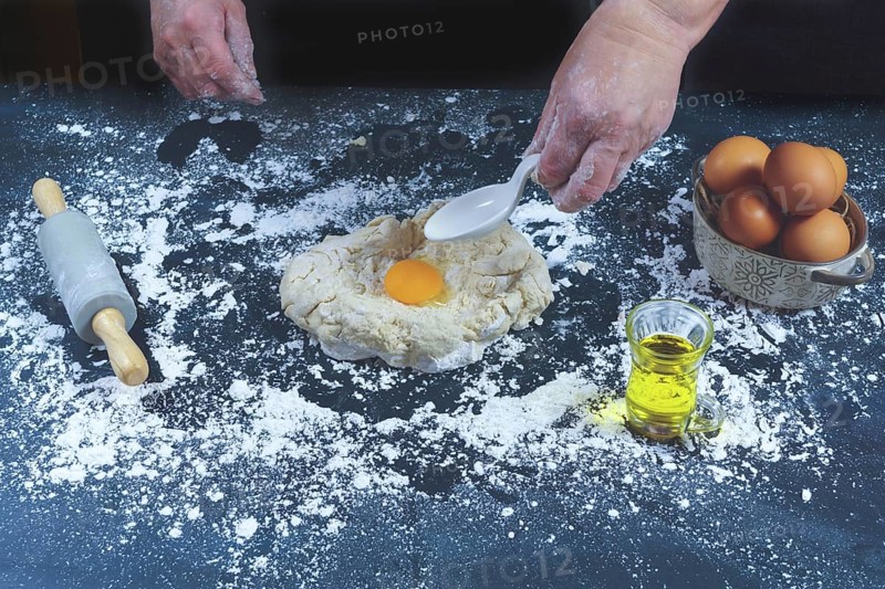 Woman adding eggs to a dough of flour to make bread on a black wooden table with olive oil