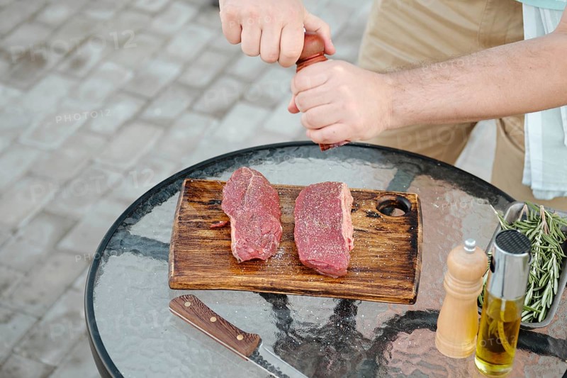 Top view of unrecognizable man seasoning raw beef steak with pepper preparing meal for grill